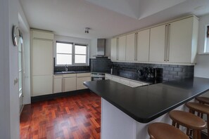 A kitchen with a black countertop, wooden floor, and white cabinets. - Beachfront Villa with Terrace & Views (Makkum)