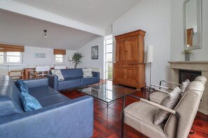 A spacious living room with a blue sofa, beige armchair, and a glass coffee table. There is a wooden cabinet and a fireplace in the background. - Beachfront Villa with Terrace & Views (Makkum)