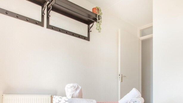 Un dormitorio con cama, radiador, una puerta y una estantería con una planta.