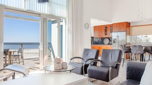 Una sala de estar moderna con balcón con vistas al mar, una cocina con armarios de madera y un comedor con taburetes de bar.