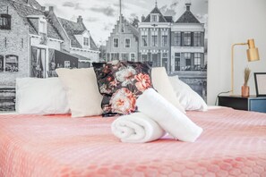 A bed with a floral pillow, a rolled white towel, and a cityscape mural in the background. - Luxury Makkum Beachvilla for 6 (Makkum)