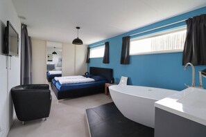 Une chambre moderne avec un grand lit, une salle de bain séparée avec une baignoire et un téléviseur fixé au mur.