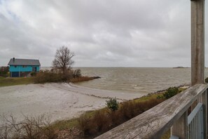 A coastal view with a house, sandy beach, and a wooden railing. - Beach Villa with Sauna for 8 Guests (Makkum)