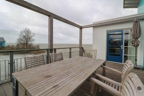 Une terrasse en bois avec une table et des chaises, une porte bleue et une vue sur la mer.