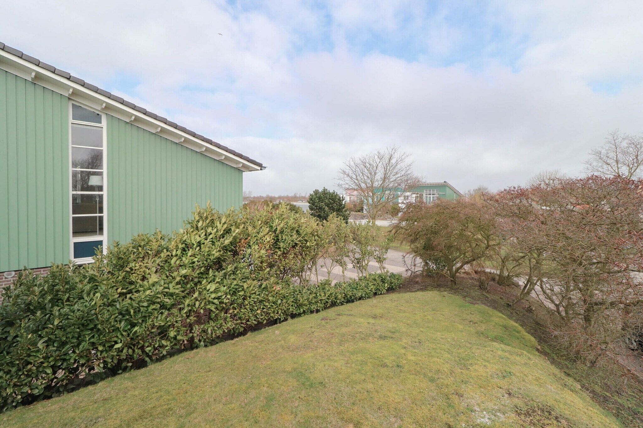 A building with a green exterior, a window, and a hedge in the foreground.