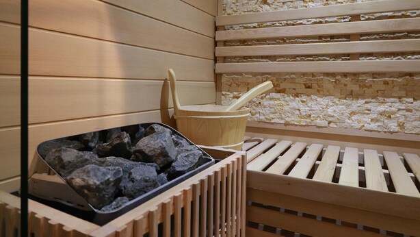 A sauna with wooden benches, a stone wall, and a bucket with a ladle. - Beach Villa with Sauna for 8 Guests (Makkum)