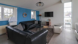 A living room with a black leather sofa, a coffee table, a TV, and a fireplace. - Beach Villa with Sauna for 8 Guests (Makkum)