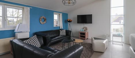 Ein Wohnzimmer mit einem schwarzen Ledersofa, einem Couchtisch, einem Fernseher und einem Kamin.