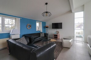 Ein Wohnzimmer mit einem schwarzen Ledersofa, einem Couchtisch, einem Fernseher und einem Kamin.