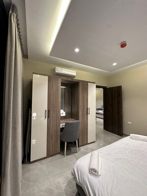A hotel room with a bed, a desk with a chair, a wardrobe, and an air conditioning unit. - 302 AL-NAJEH JRE Apartments For Rent ave (Amman)