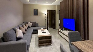 Ein modernes Wohnzimmer mit einem Ecksofa, einem Couchtisch, einem Fernseher und einem Essbereich.