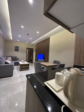 A modern living room with a sofa, a coffee table, and a dining area with chairs and a table. - 302 AL-NAJEH JRE Apartments For Rent ave (Amman)