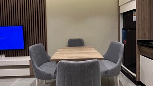Eine moderne Küche mit einem Holzesstisch, zwei grau gepolsterten Stühlen, einem Einbaufernseher und einem Kühlschrank.