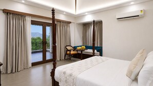 A hotel room with a four-poster bed, a balcony with curtains, a dining table with chairs, and an air conditioning unit. - Aamba Bagh Resort Kumbhalgarh  (Kumbhalgarh)