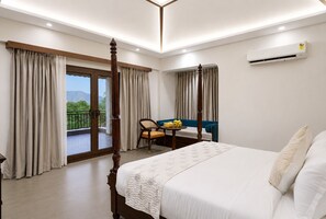 A hotel room with a four-poster bed, a balcony with curtains, a dining table with chairs, and an air conditioning unit. - Aamba Bagh Resort Kumbhalgarh  (Kumbhalgarh)