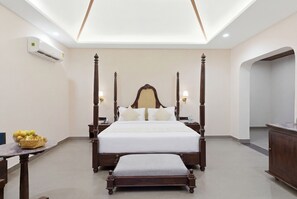 Habitación de hotel con cama con dosel, una mesita de noche con lámpara, una pequeña mesa con frutero y un equipo de aire acondicionado en la pared.