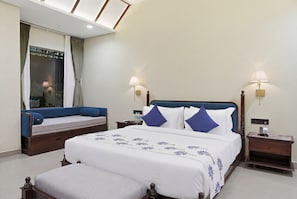 A hotel room with a large bed, a sofa, two bedside tables with lamps, and a view of a balcony. - Aamba Bagh Resort Kumbhalgarh  (Kumbhalgarh)