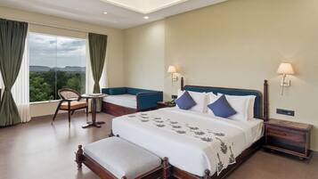 A hotel room with a large bed, a small table, a chair, and a view of the outdoors.