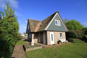 A small, single-story house with a steeply pitched roof, a front door, and a small porch area. - Deluxe Beach Villa with Garden (Makkum)