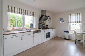 A kitchen with white cabinets, a stainless steel sink, and a gas stove. - Deluxe Beach Villa with Garden (Makkum)