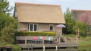 Ett traditionellt hus med ett halmtak, en träbrygga och en liten båt.