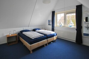 A bedroom with two beds, a bedside table, a window with curtains, and a radiator. - Deluxe Beach Villa with Garden (Makkum)