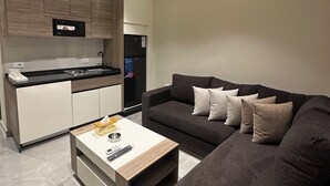 Ett modernt vardagsrum med en mörkgrå soffa, ett vitt soffbord och en köksdel med träskåp och en inbyggd mikrovågsugn.