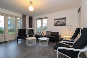 A modern living room with a sofa, two lounge chairs, a TV, and a fireplace. - Beach Villa with Garden & Water Access (Makkum)