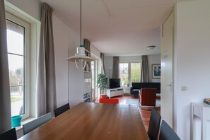 A modern living room with a wooden dining table, a TV, a sofa, and a plant. - Detached Spacious Beach Villa for 8 (Makkum)