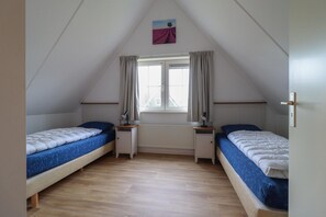 A dormitory room with two single beds, a window with curtains, a radiator, and a small painting on the wall. - Detached Spacious Beach Villa for 8 (Makkum)