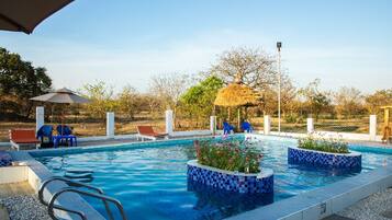 Piscina com borda em azulejo, cadeiras de descanso e estrutura de palha.