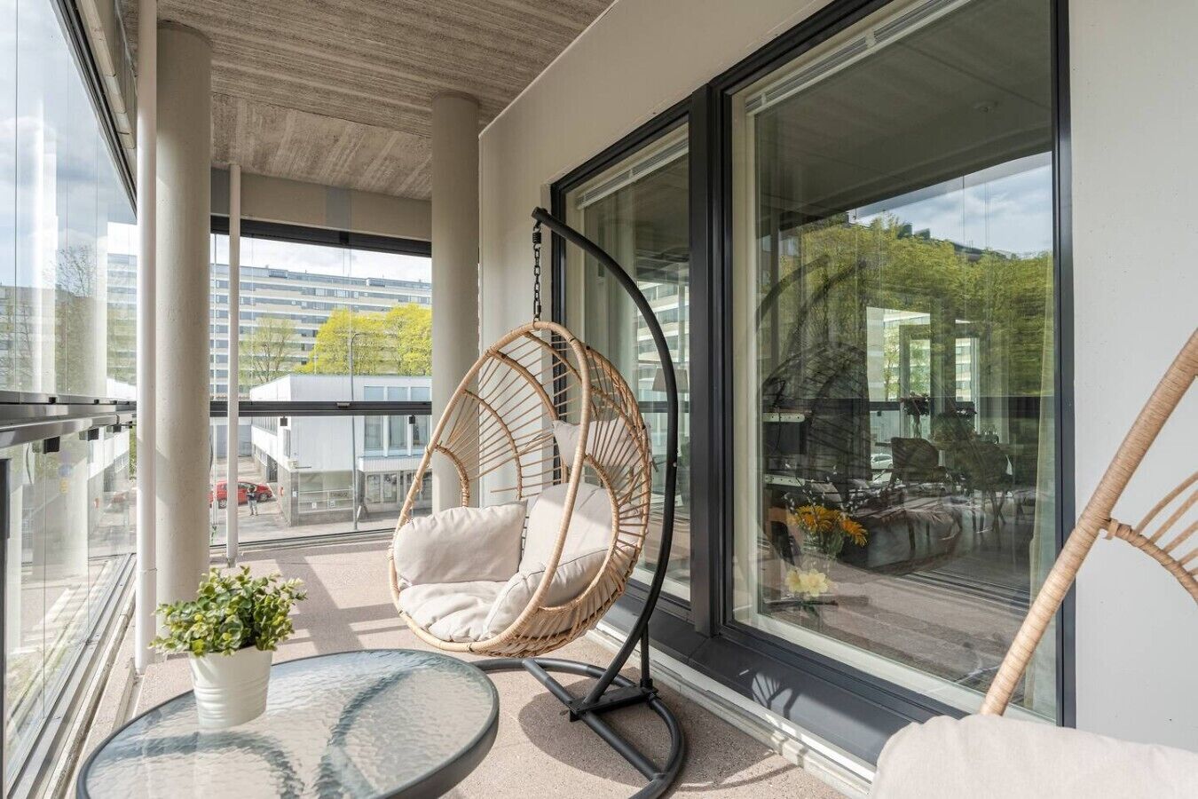 A balcony with a wicker chair, a glass table, and a potted plant.
