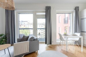 Een modern appartement met een grijze bank, een eettafel met stoelen en grote ramen met grijze gordijnen.