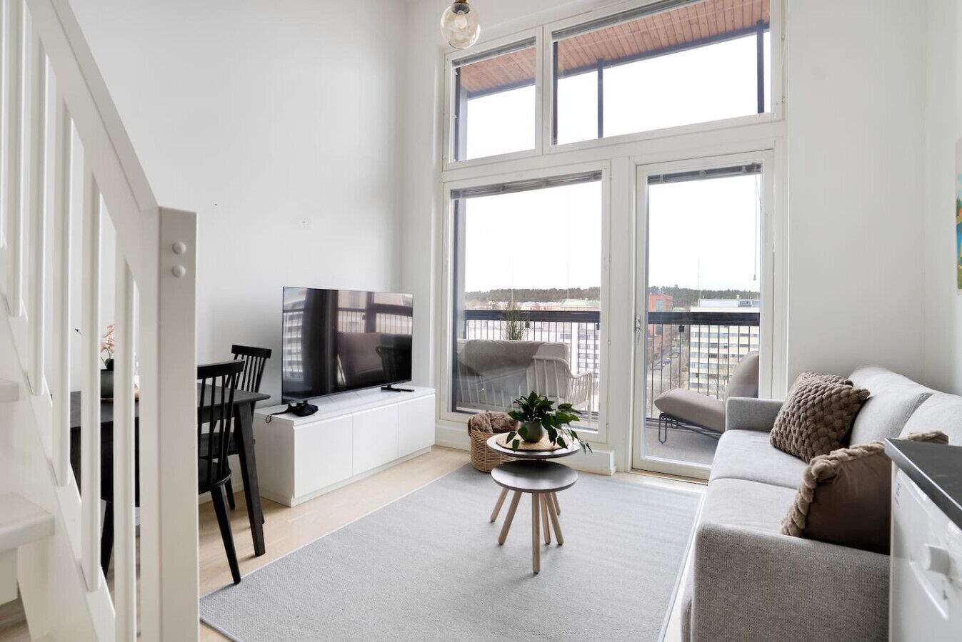 A modern living room with a flat-screen TV, a sofa, a coffee table, and a balcony with a view.