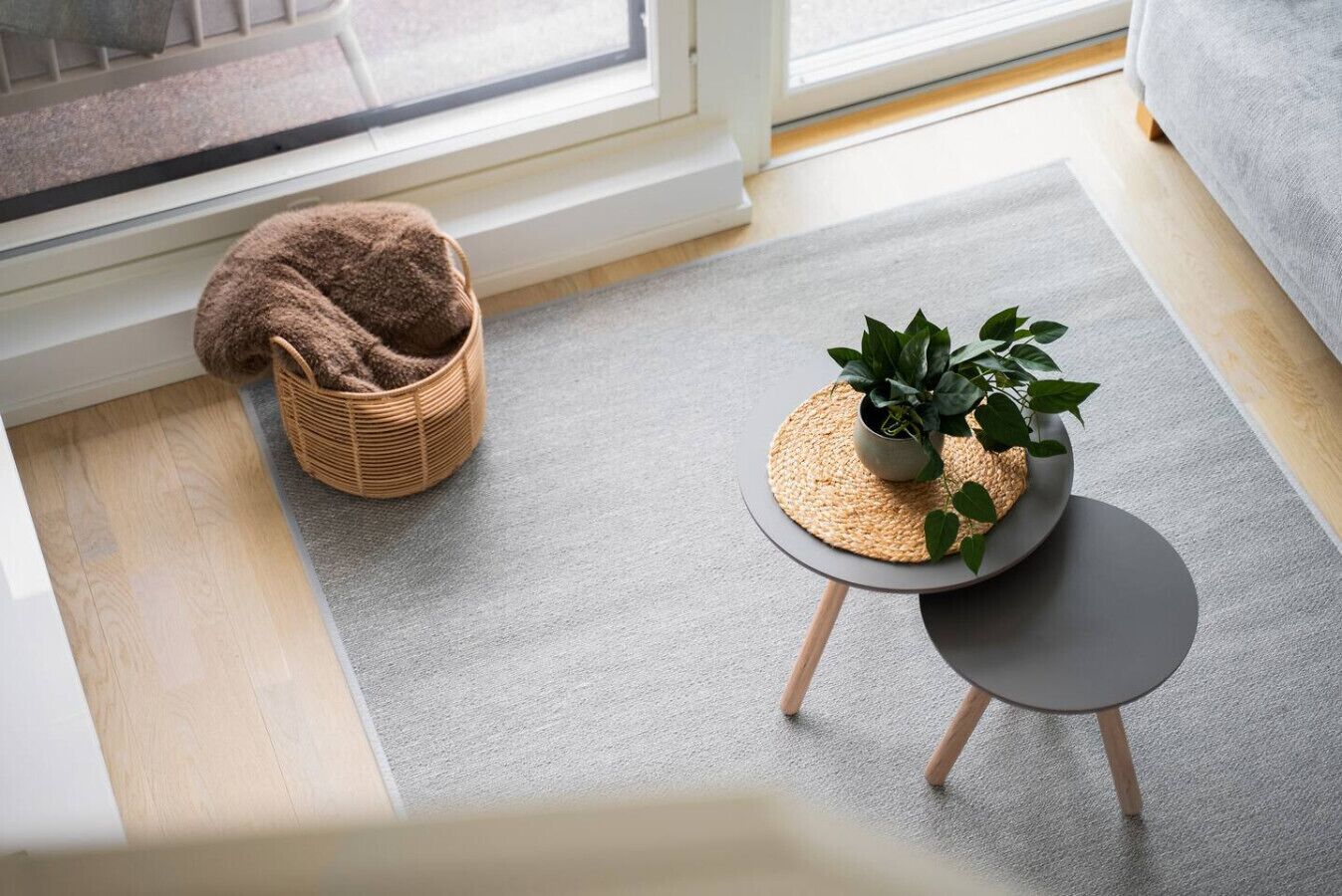 A room with a grey carpet, a wicker basket, and a small round table with a plant.