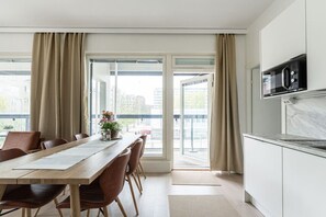 A modern kitchen with a microwave, a dining area with a wooden table and chairs, and large windows with curtains.