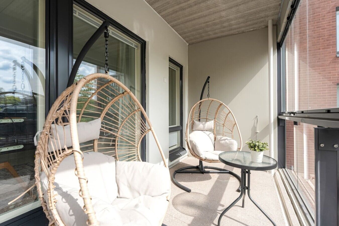 A balcony with two wicker chairs, one with a cushion and the other with a cushion and a small table.