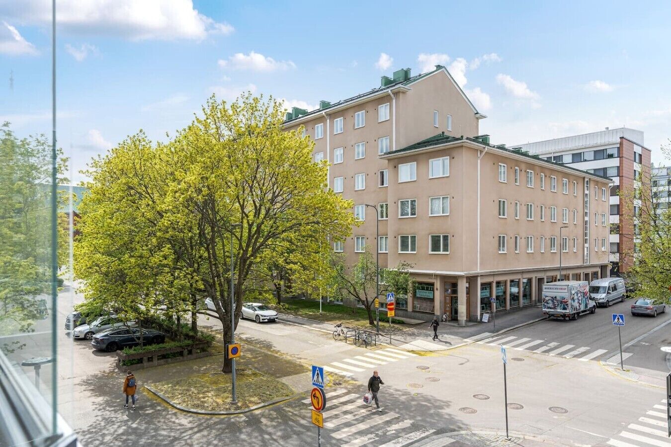 A multi-story building with a flat facade, a pedestrian crossing, and a tree in the foreground.