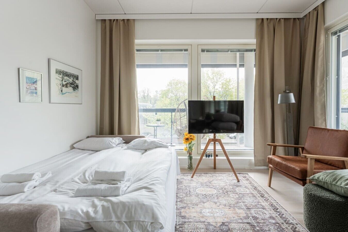 A hotel room with a bed, a TV on a stand, a chair, and a window with curtains.