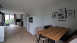 Eine moderne Küche mit Einbaukühlschrank, ein Essbereich mit Holztisch und -stühlen sowie ein Blick ins Freie.