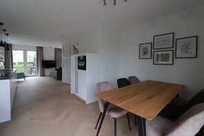Eine moderne Küche mit Einbaukühlschrank, ein Essbereich mit Holztisch und -stühlen sowie ein Blick ins Freie.