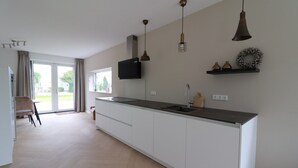 Eine moderne Küche mit einer großen Kochinsel, Pendelleuchten und Blick ins Freie.