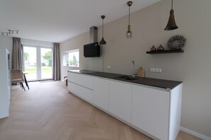 Eine moderne Küche mit einer großen Kochinsel, Pendelleuchten und Blick ins Freie.