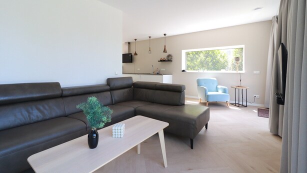 Ein modernes Wohnzimmer mit einer Eckcouch, einem Couchtisch, einem blauen Sessel und einer Küche im Hintergrund.