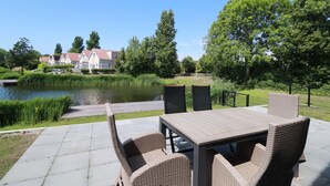 Eine Außenpatio mit Tisch und Stühlen, einem Teich und einem Zaun.