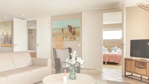 Un salon comprenant un canapé, une table basse, un tableau, un fauteuil et un téléviseur.