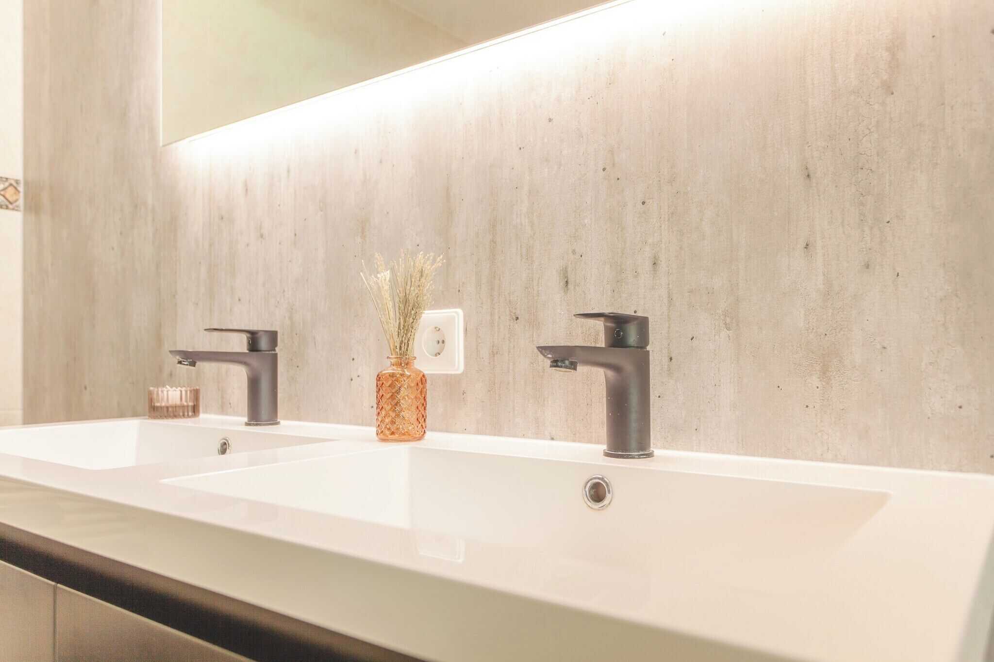 A modern bathroom with two sinks, a large mirror, and a decorative vase.