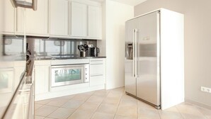 Une cuisine moderne avec des armoires blanches, des appareils électroménagers en acier inoxydable et un sol carrelé.