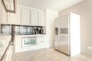 Een moderne keuken met witte kasten, roestvrijstalen apparatuur en een betegelde vloer.