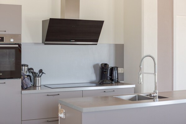 A modern kitchen with a built-in oven, a coffee maker, and a stainless steel sink.